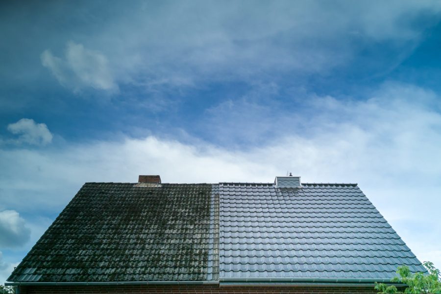 A roof with half clean metal shingles and half coated with black algae.
